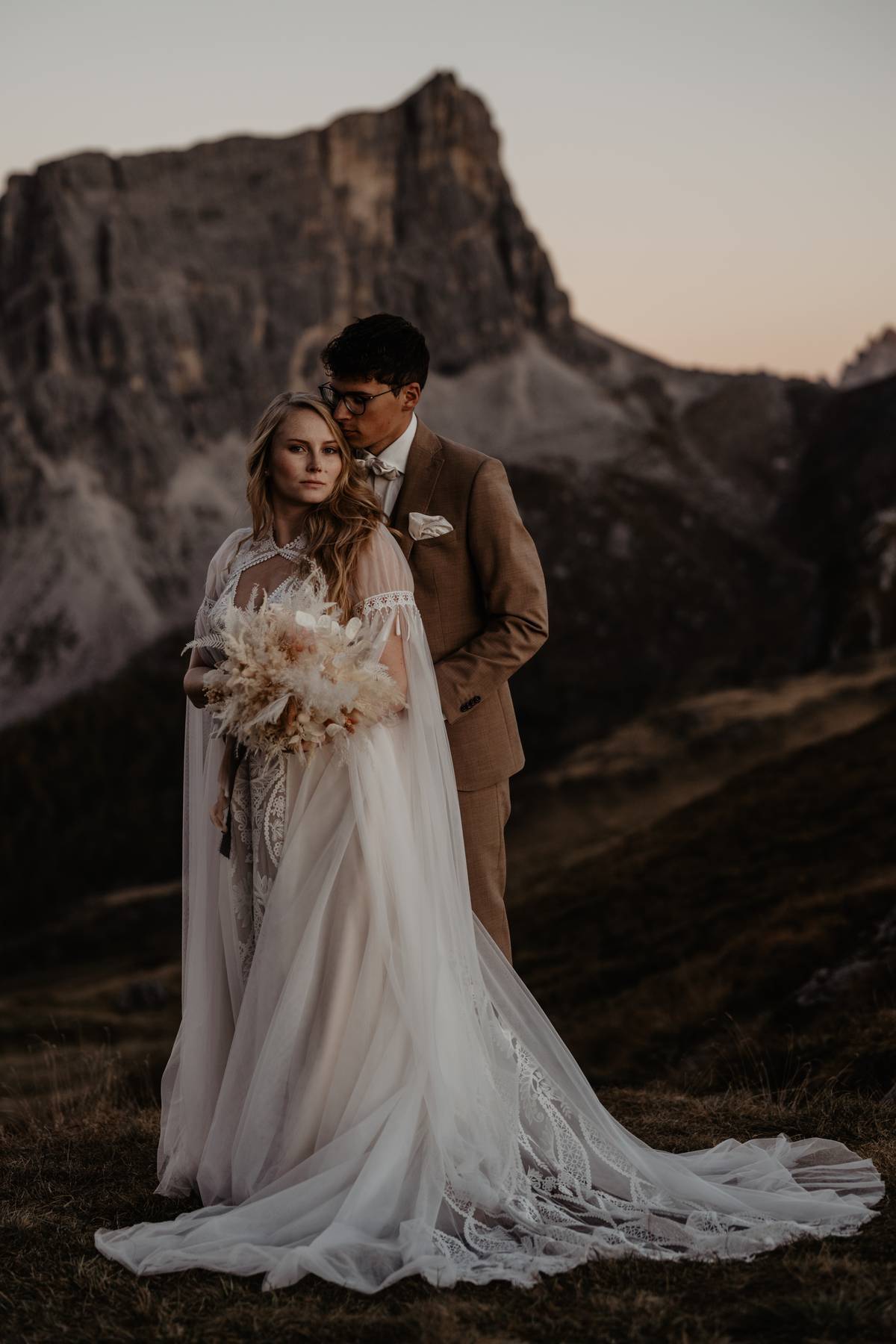 Elopement couple in wedding attire in the Dolomites, Italy, standing close with dramatic mountain rock behind