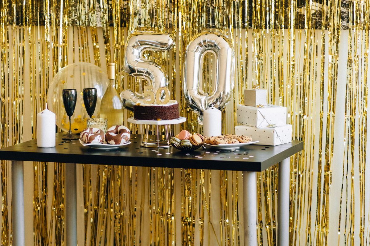 Pidulik juubelilaud kuldsete dekoratsioonide, tordi ja number 50 õhupallidega