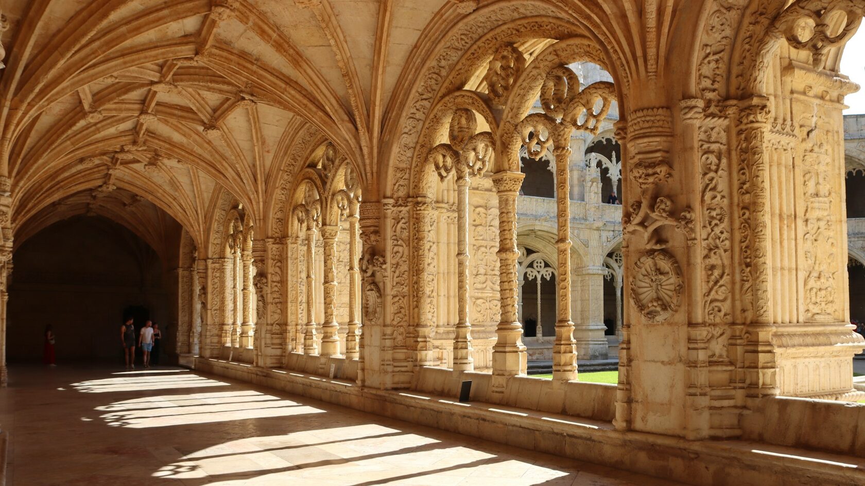The carved stone cloister of the Jerónimos Monastery in Lisbon, soft golden light falling through the arches