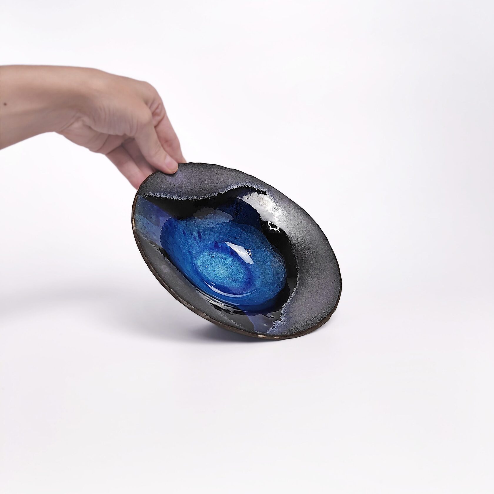 Handmade decorative ceramic plate with deep blue glossy glaze and black clay base