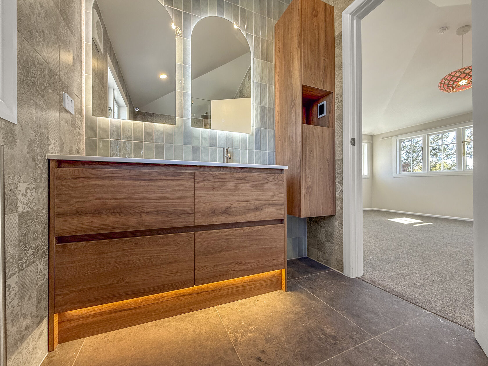 Timber bathroom vanity beside a frosted window and grey wall tiles