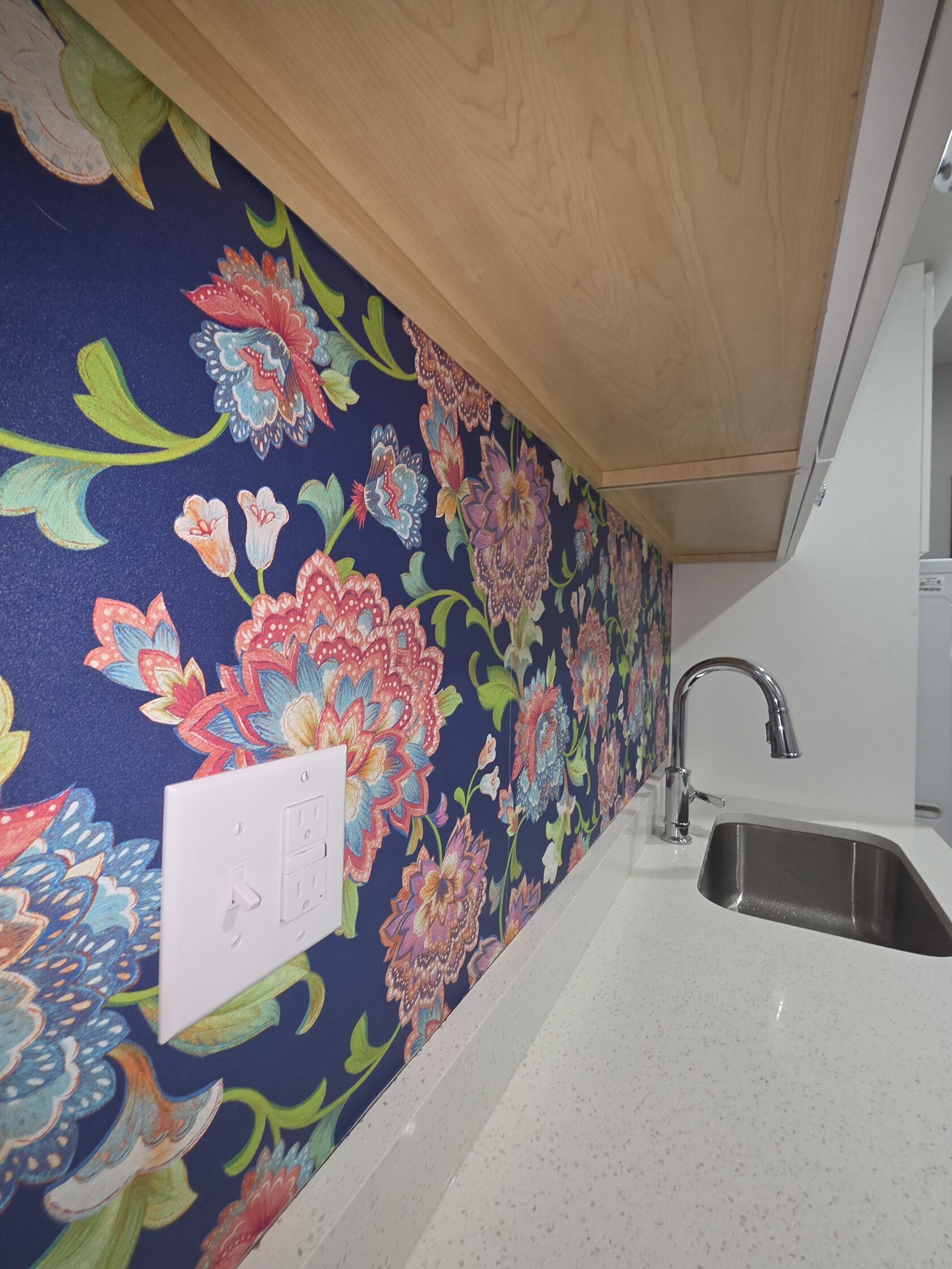 Colorful floral wallpaper installed around a kitchen outlet, backsplash and sink