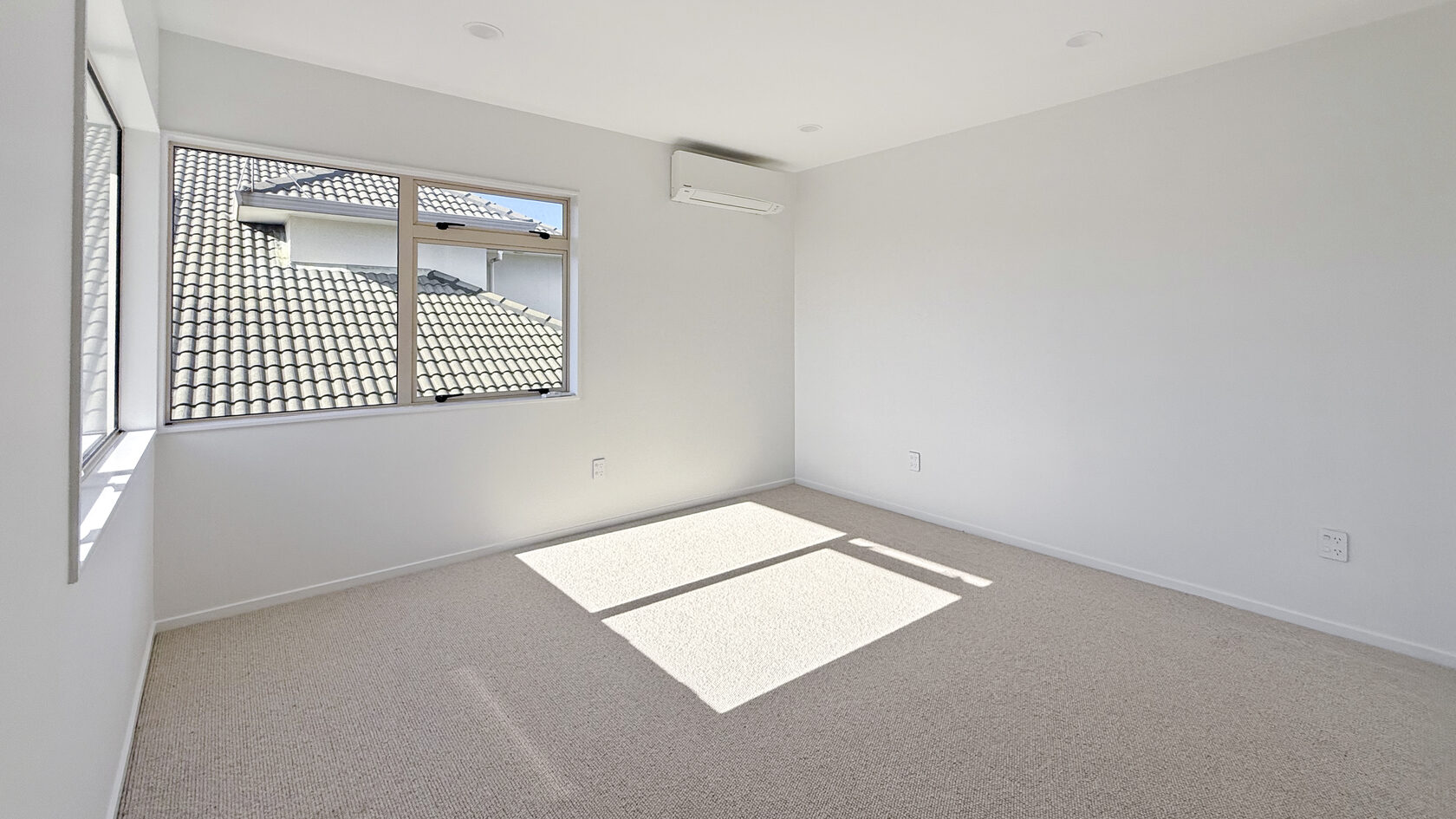 Bright St Heliers bedroom with new carpet, large windows and a wall-mounted heat pump.