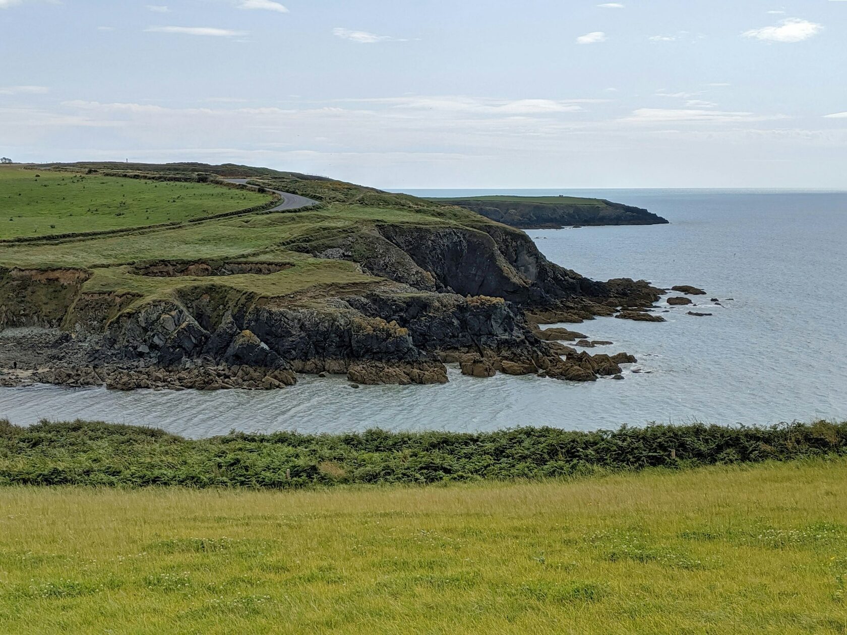 A golf links on a dramatic Atlantic headland in Ireland, green fairways running to the cliff edge under golden evening light.