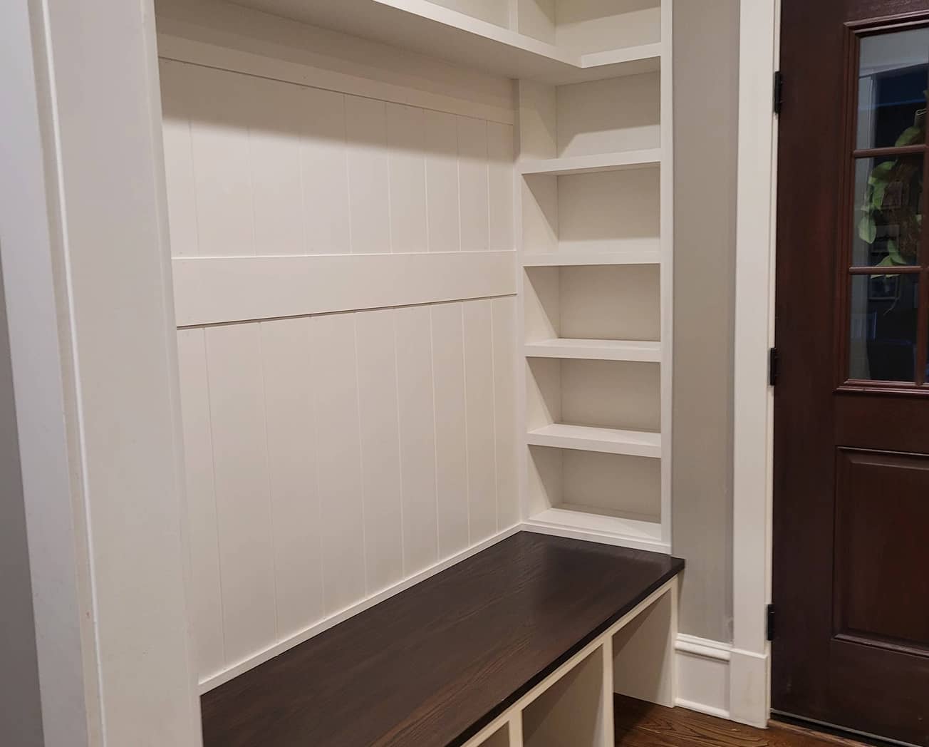 Mudroom shelves and built-in dark stained bench furnished with baskets and hooks 