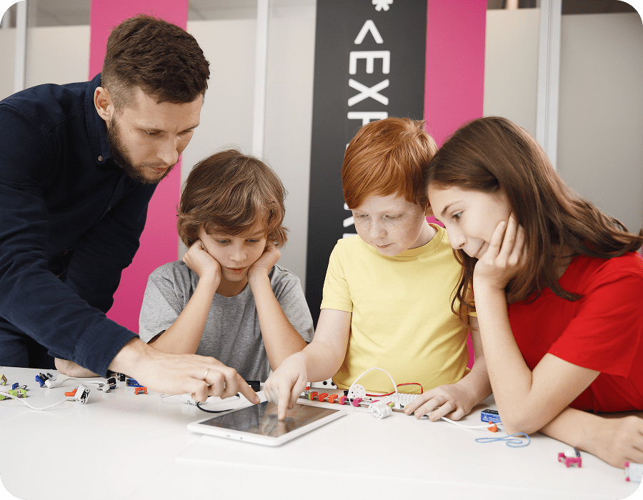 A teacher and three children building an electronic gadget together, with a tablet on the table, at Impact Academies in Amsterdam
