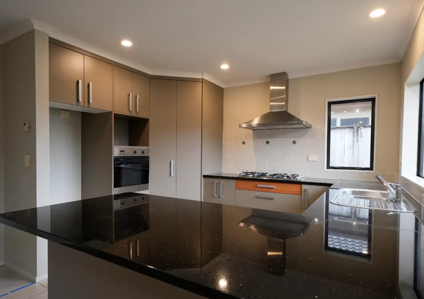 Before: Original kitchen with beige cupboards, black benchtops, built-in oven, gas hob and stainless steel sink