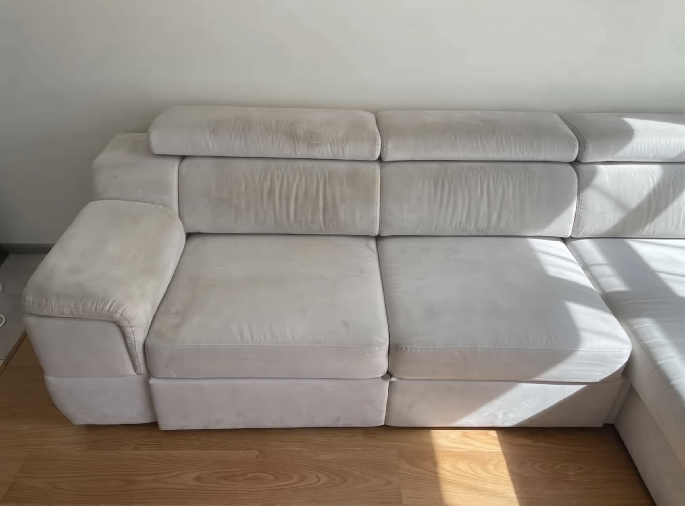 Breites wei&szlig;es Ecksofa aus hochwertigem Stoff vor der Reinigung, mit grauem Schleier, dunkleren Sitzpl&auml;tzen und sichtbaren Gebrauchsspuren. Die Kundin hat das Foto selbst aufgenommen und ihrer Google-Bewertung f&uuml;r Shikardos Reinigung in Frankfurt beigef&uuml;gt.