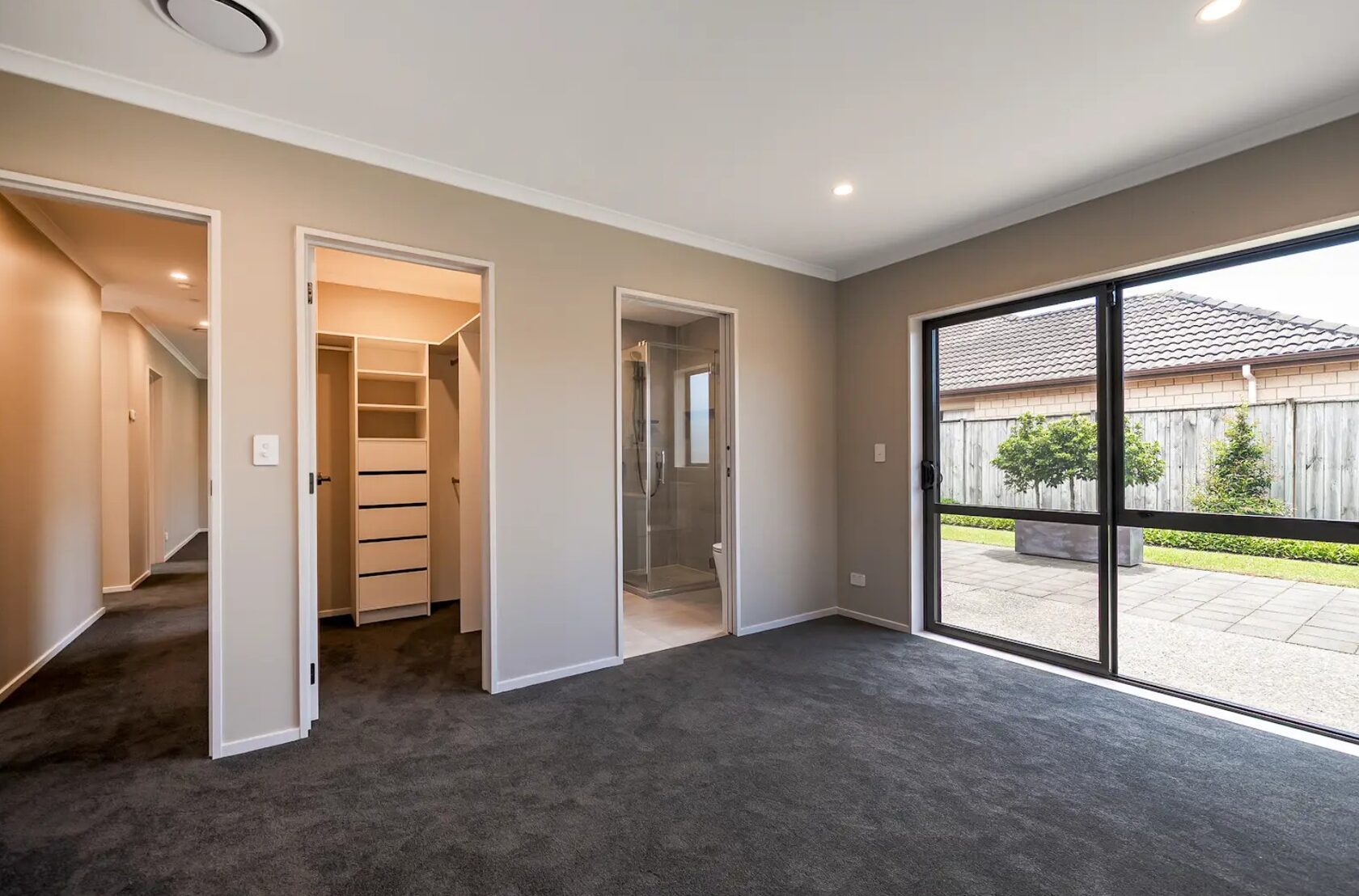 Carpeted room with doors to a walk-in wardrobe and bathroom and sliding glass doors opening to a patio