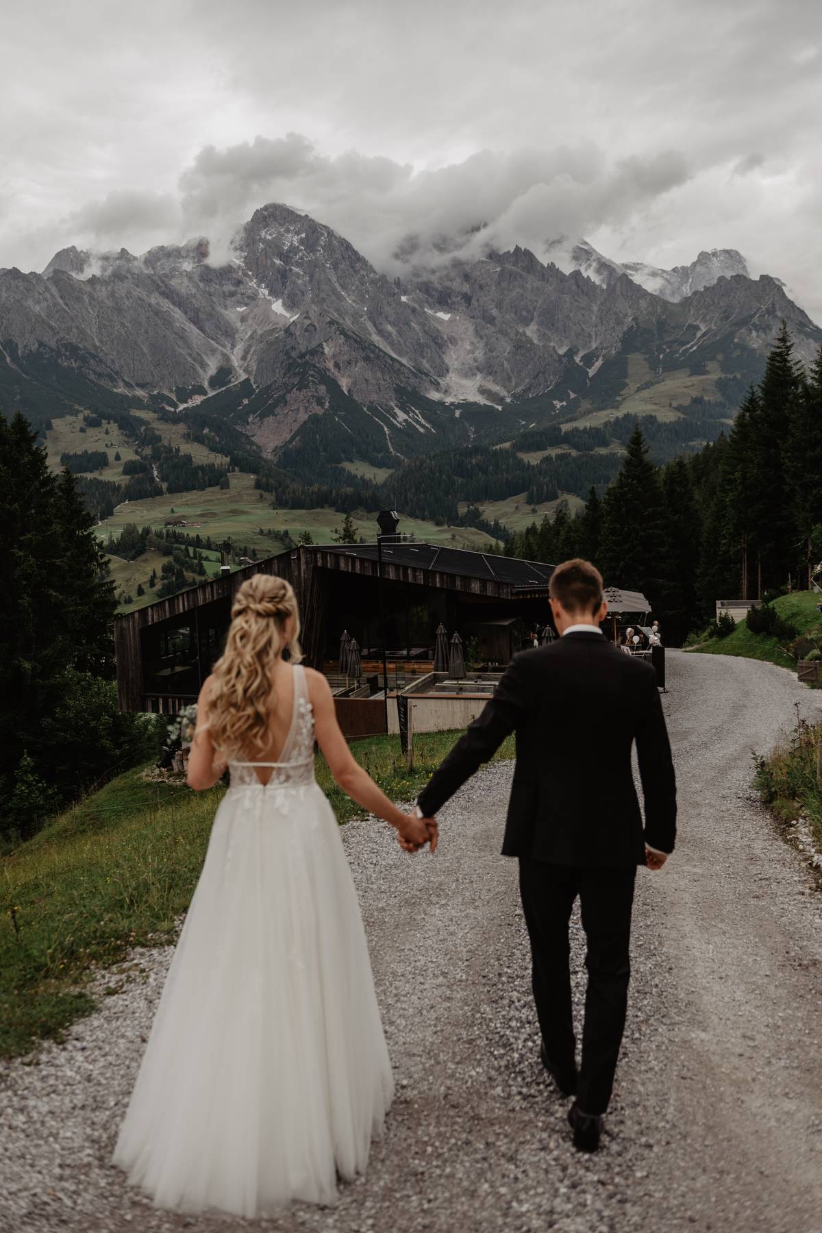 Bride and groom walking hand in hand on a mountain path in the Austrian Alps, dramatic peaks ahead