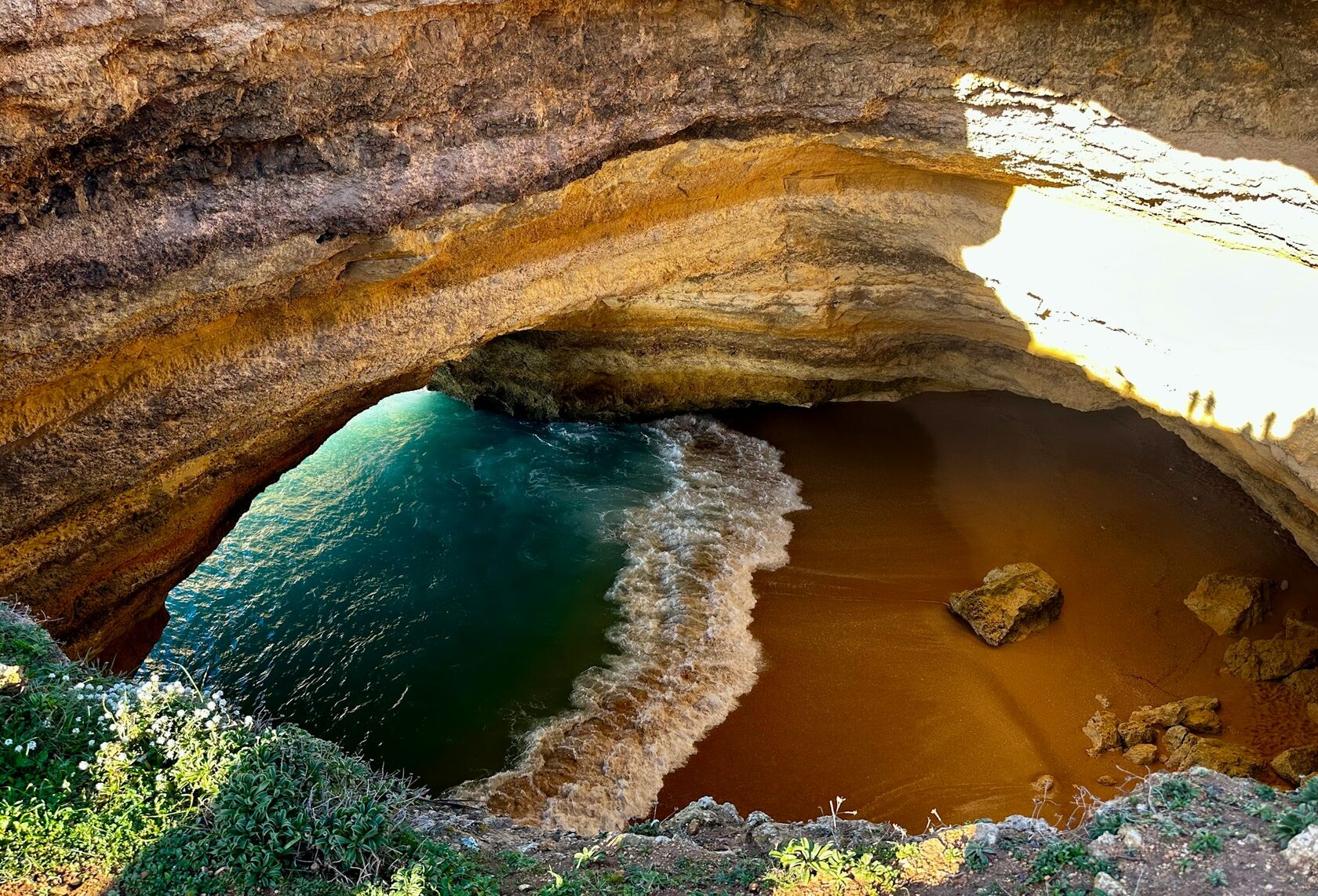 Sunlight pouring through the open roof of the Benagil sea cave onto its golden beach
