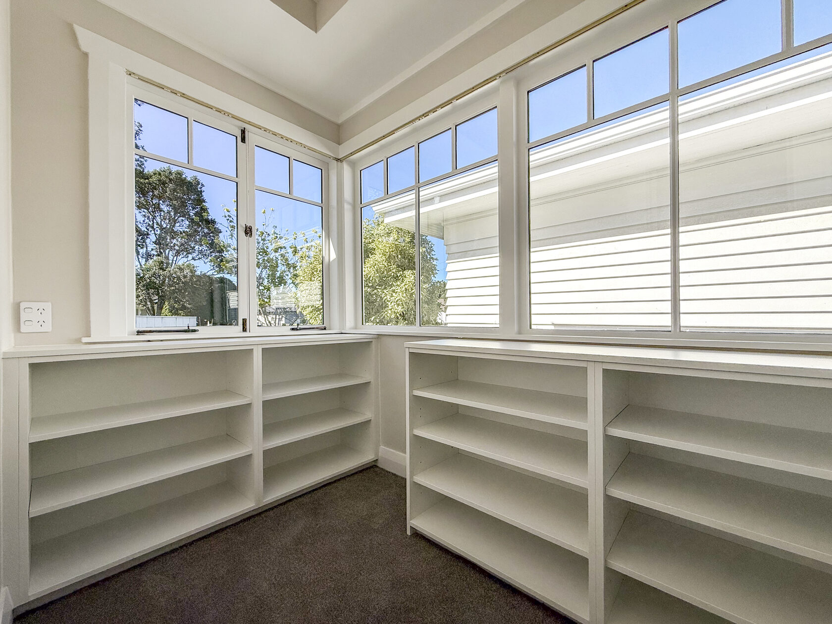 White built-in shelving beneath timber-framed windows in a carpeted room
