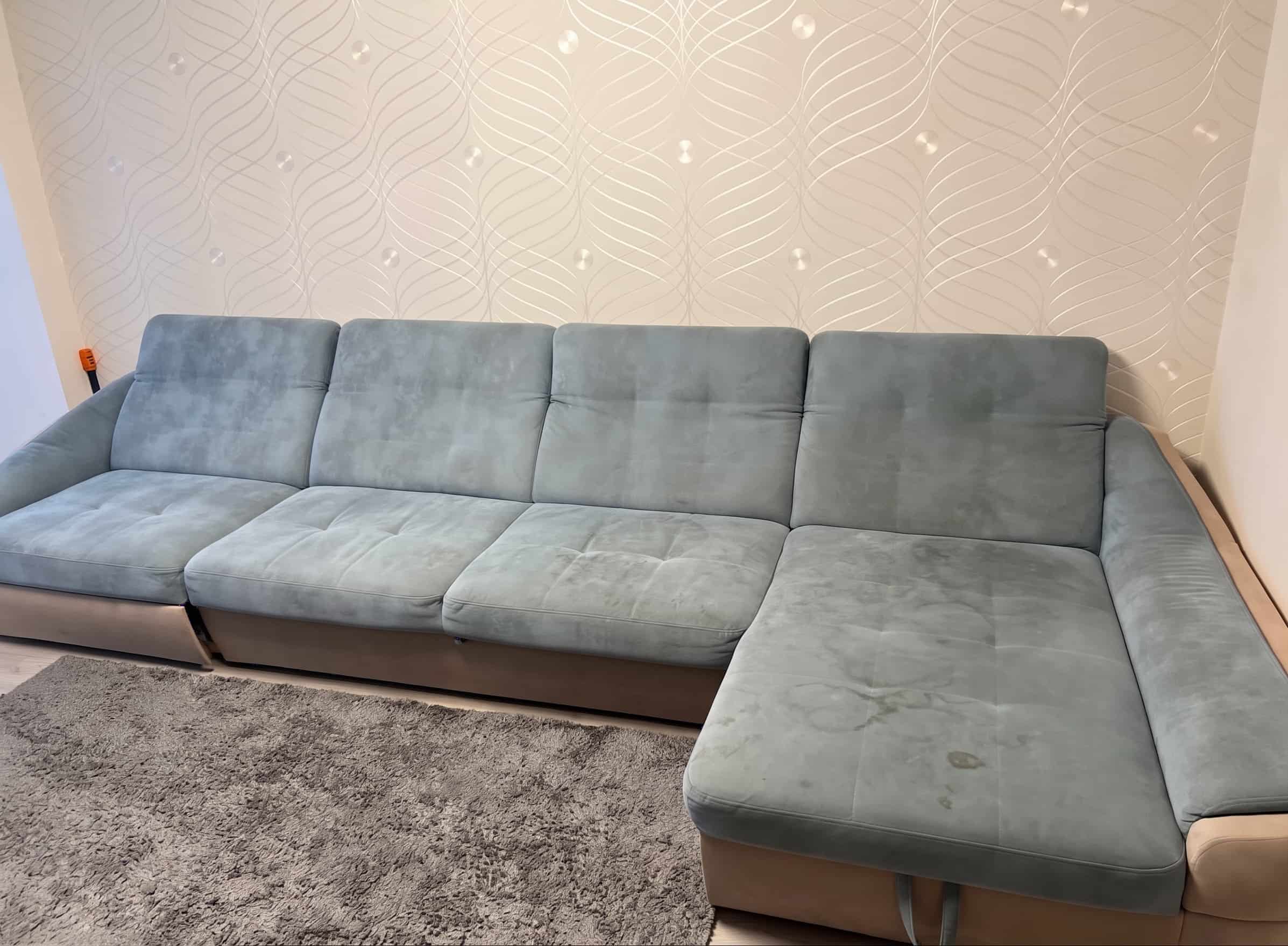 Verschmutztes blaues Samtsofa mit Flecken in einem hellen Wohnzimmer vor der Polsterreinigung in Frankfurt
