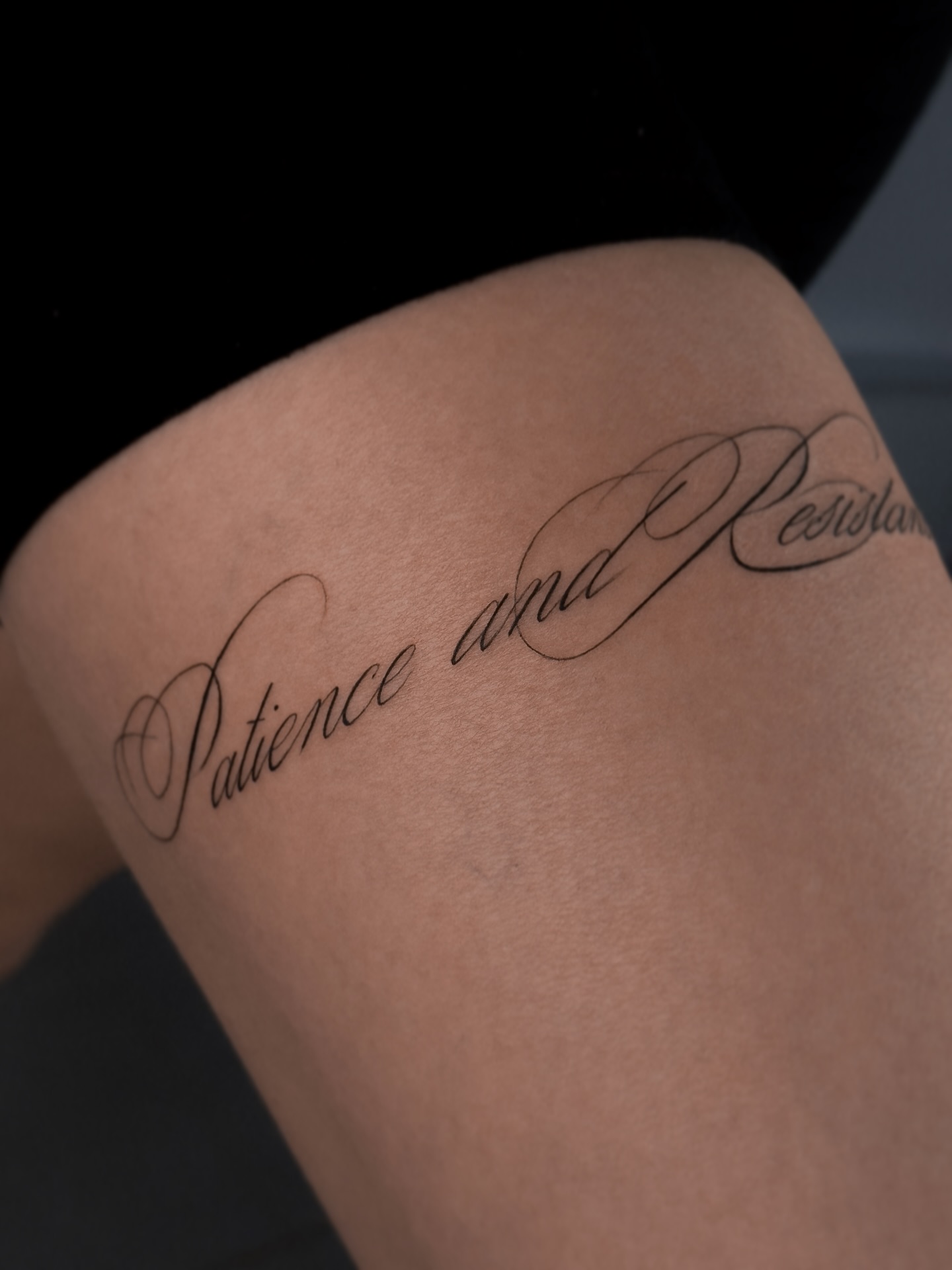 Delicate calligraphic lettering tattoo with long flowing strokes on the upper arm by @zaitceva.ana
