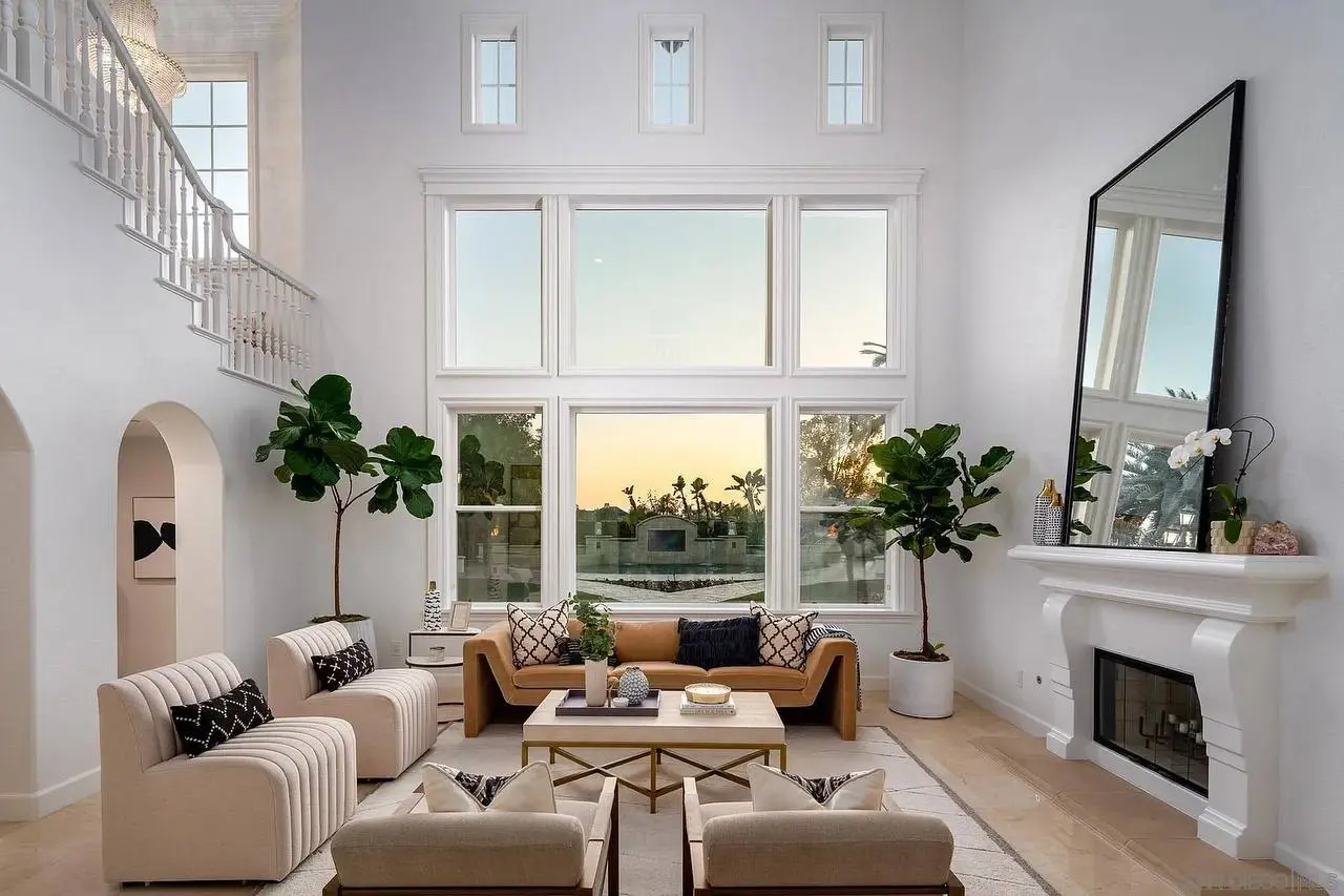 Two matching fiddle-leaf figs flanking a fireplace in a two-story living room with a floating staircase