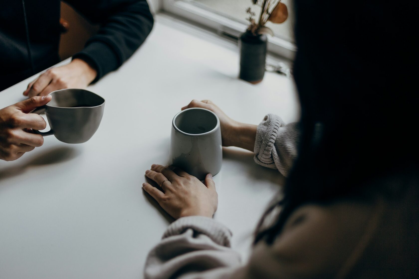Conversación cercana entre dos personas alrededor de una mesa, en un plano cerrado sin rostros visibles