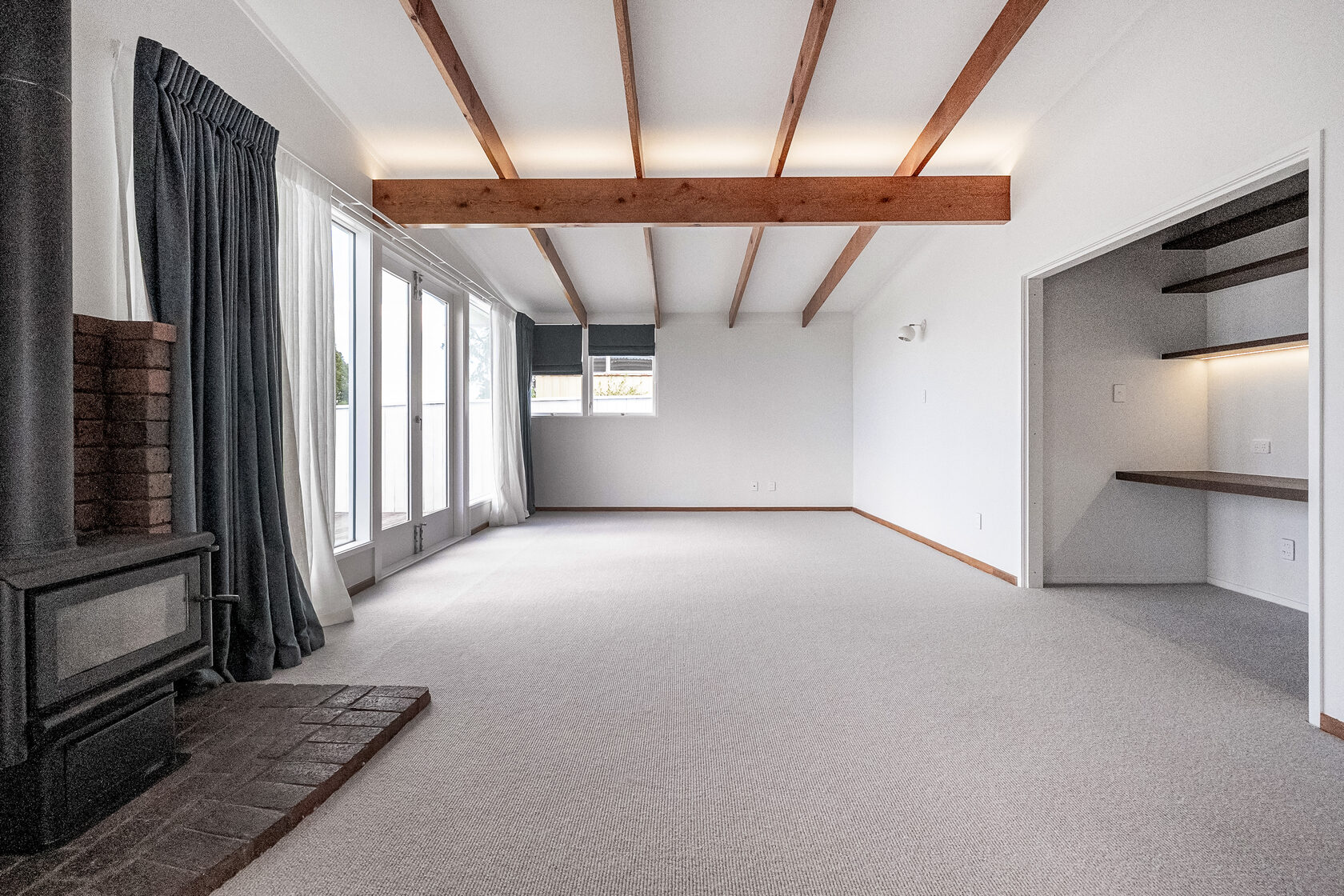 Renovated Hillcrest living room with exposed timber beams, light carpet, a wood burner and a built-in desk nook