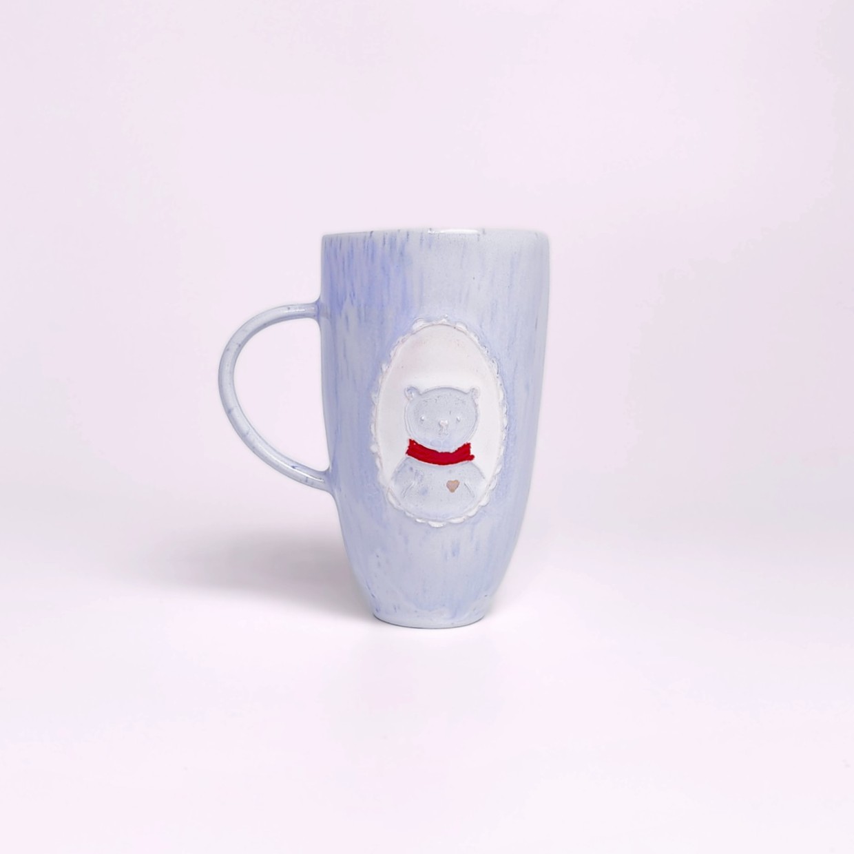 Unique handmade light blue ceramic mug with a pastel glaze, adorned with a sculpted medallion of a cute bear in a red scarf