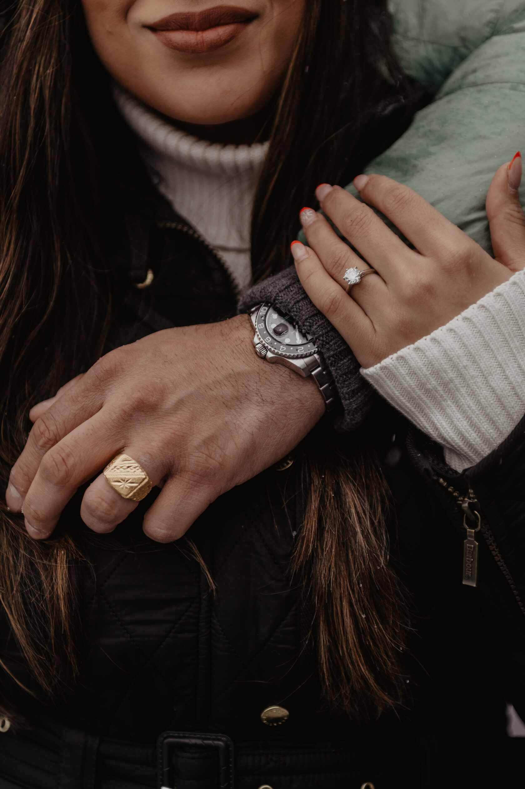 Close-up of an engagement ring on her hand wrapped around her partner’s arm during a winter couple session