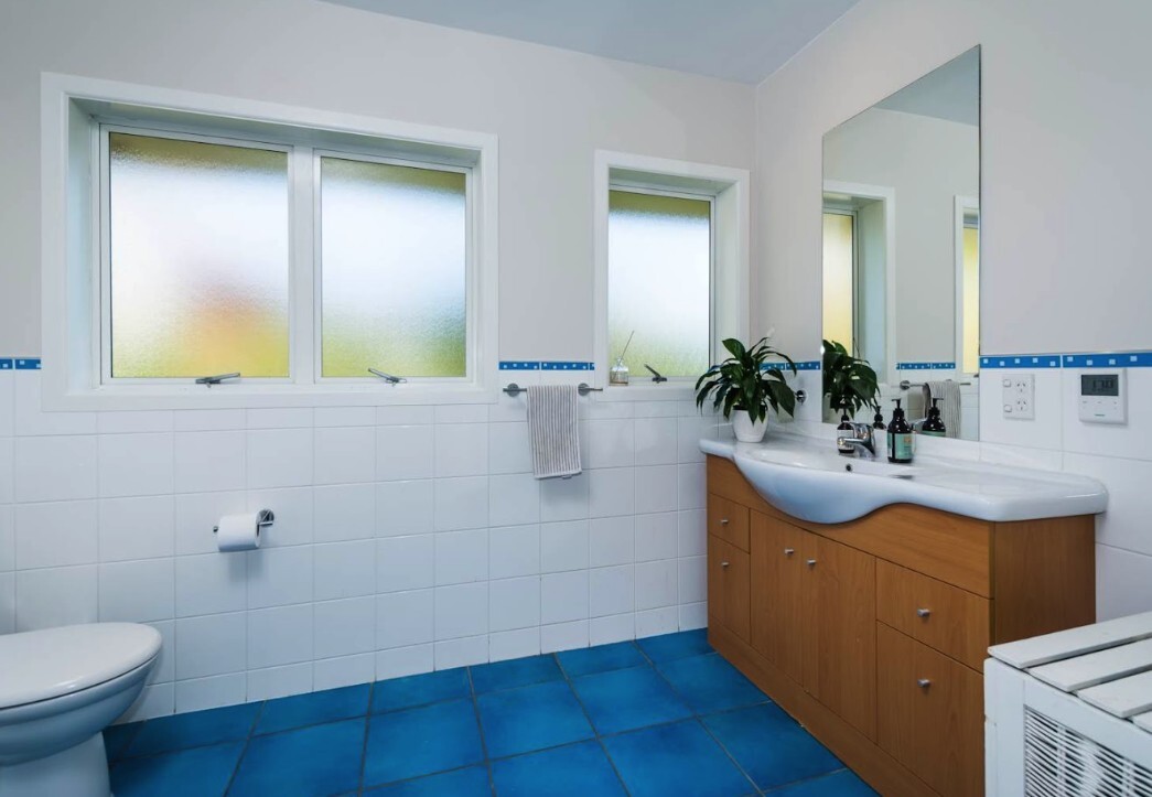 Before: original Glenfield bathroom with blue floor tiles and timber vanity