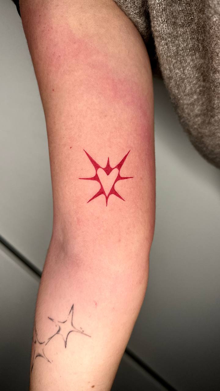 Red heart-and-star tattoo by Lisa on the forearm.