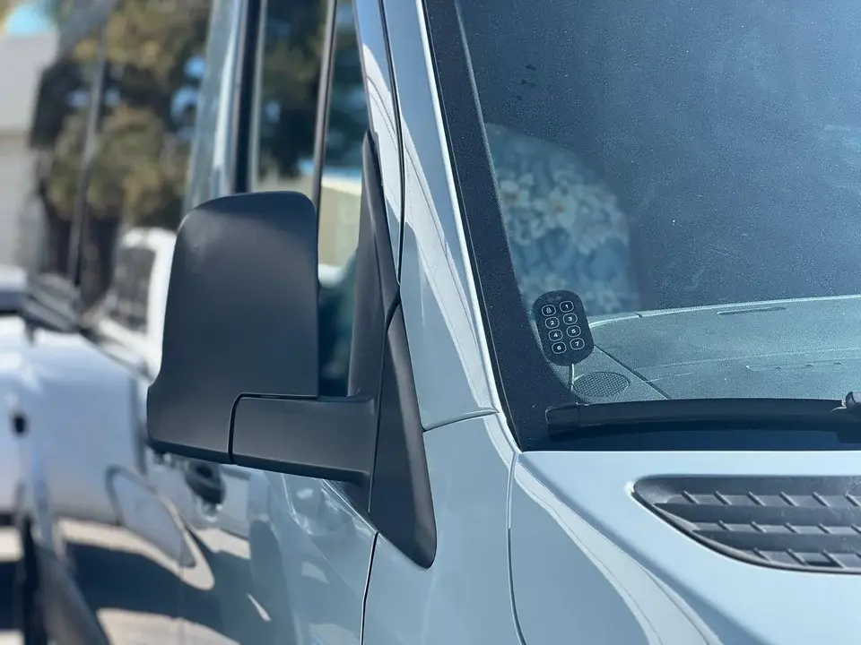 Keyless touchpad visible through the windshield of a white Sprinter van beside the side mirror.