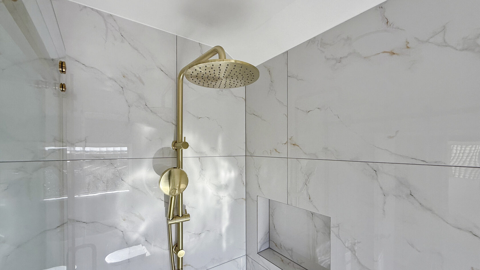 Brushed brass rainfall shower, marble-look wall tiles and a built-in niche in St Heliers.