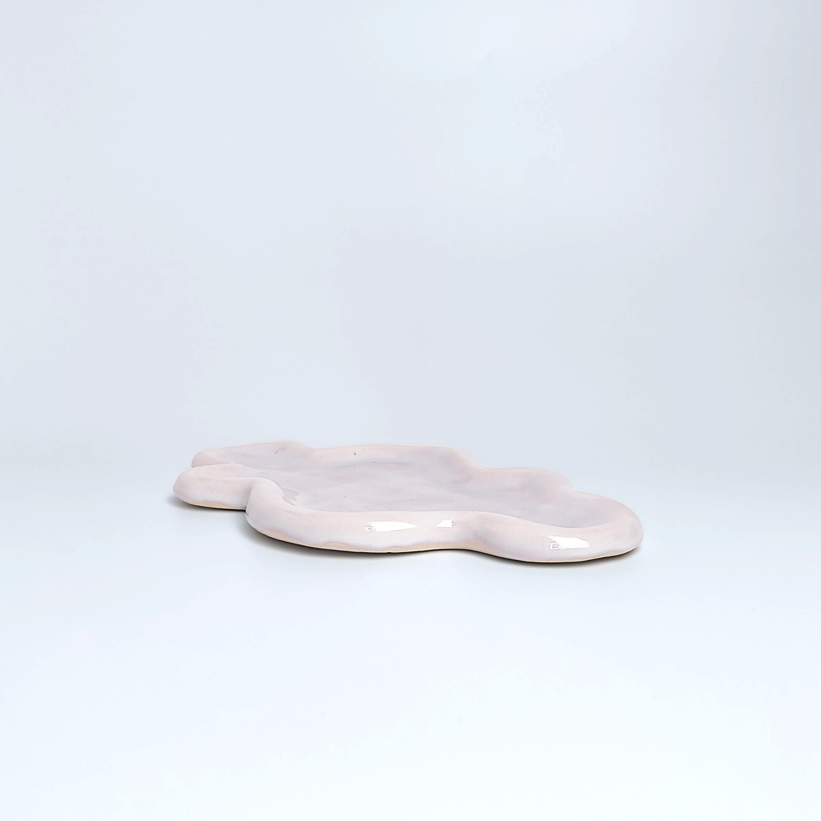 Unique handmade ceramic plate shaped like a cloud, featuring soft pastel pink glazing and an organic sculptural form