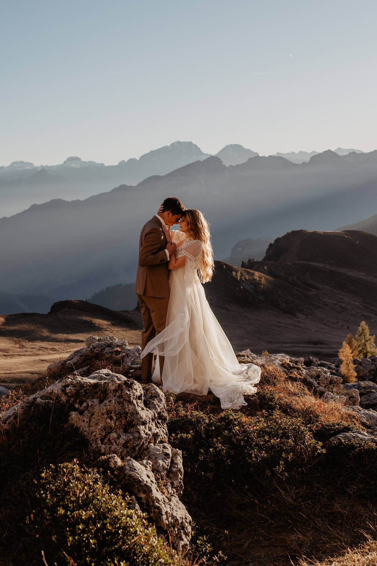 Elopement couple embracing on a rocky viewpoint in the Dolomites, Italy, soft evening light and layered mountains