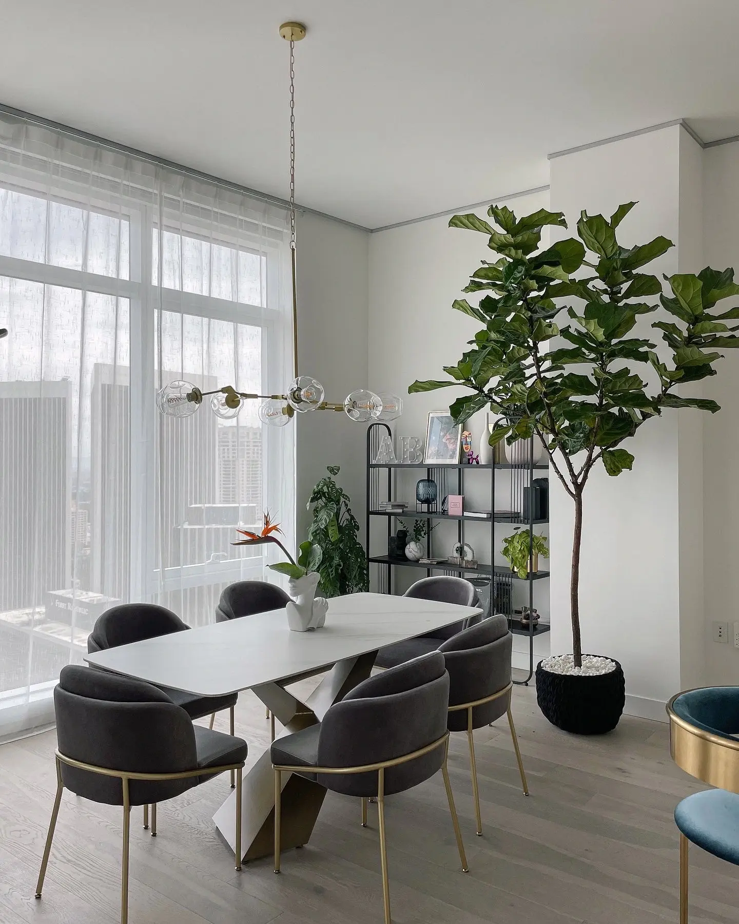 A fiddle-leaf fig near a shelving unit in a high-rise dining room with a bird of paradise centerpiece on the table