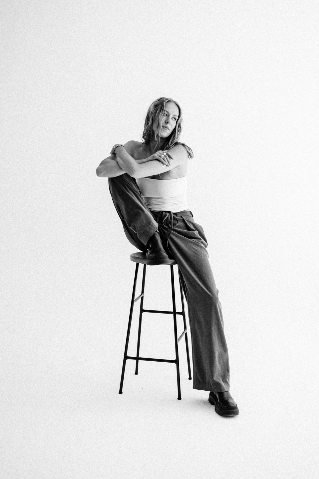 Model im weißen Top und weiter Hose auf einem hohen Hocker, ein Knie angezogen