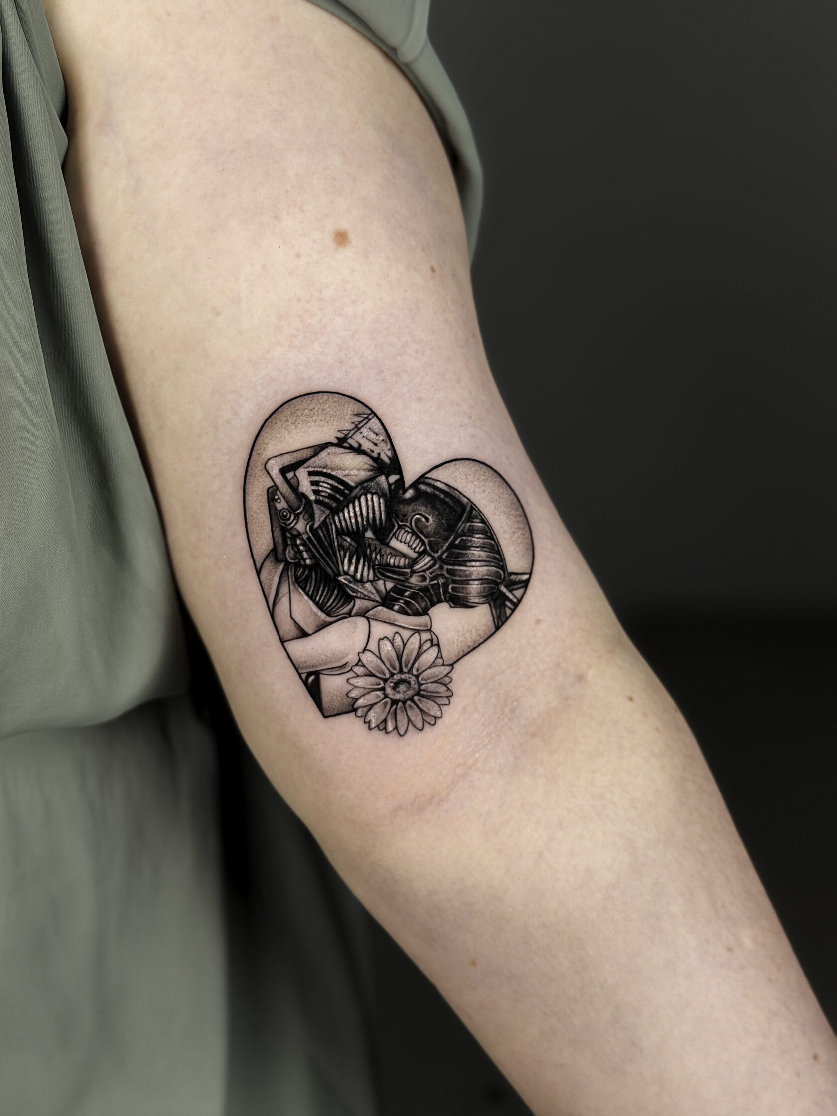 Black-and-Grey-Cover-Up mit Figuren und Blüte in Herzform am Oberarm