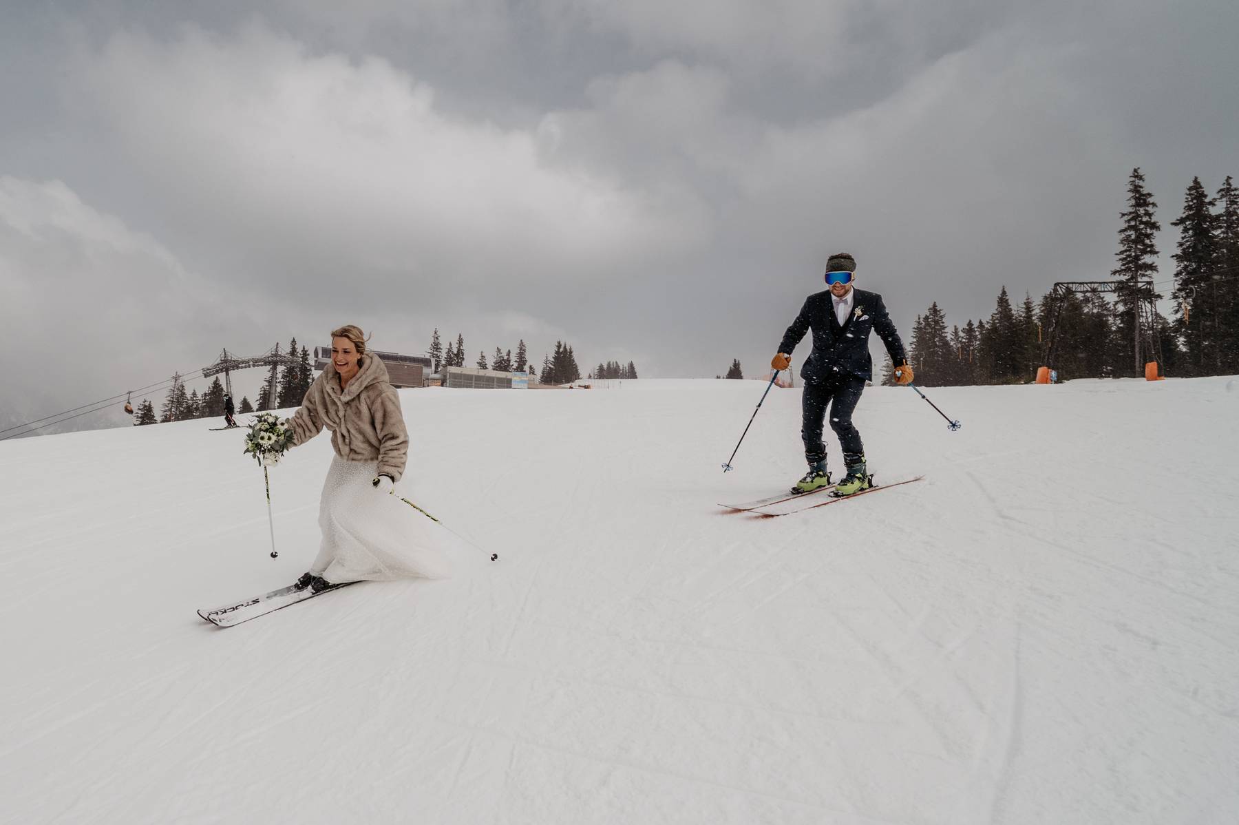 Bride and groom skiing down a snowy mountain slope in their wedding attire during their wedding adventure in Dienten am Hochkönig