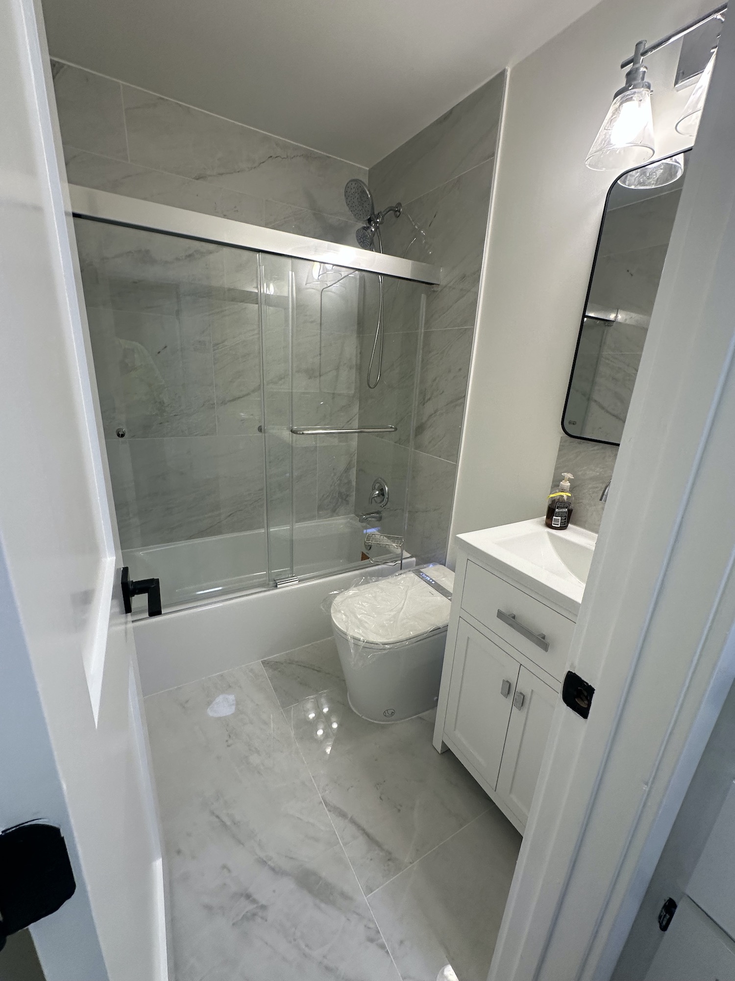 Completed Austin bathroom renovation viewed from doorway with vanity, smart toilet, bathtub and glass panel