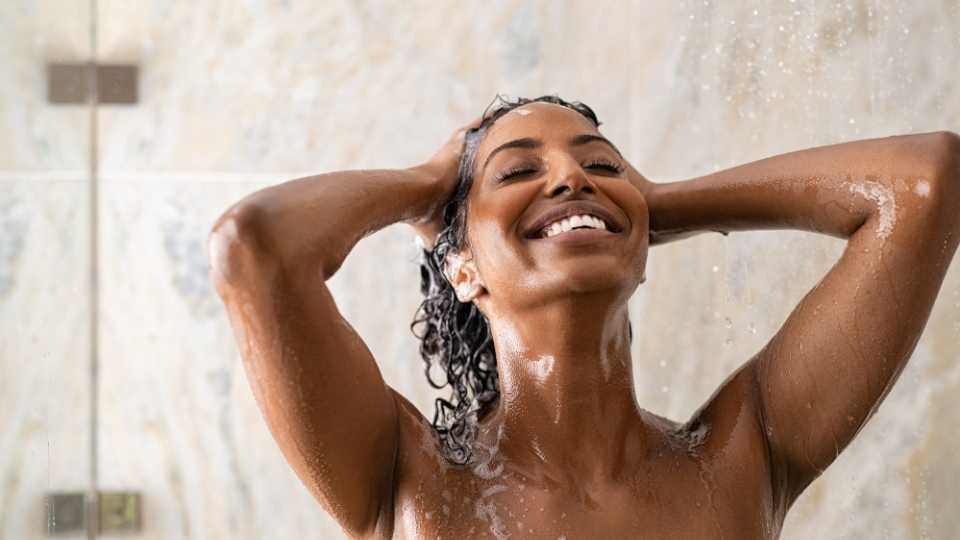 The image shows a woman enjoying a shower, highlighting the benefits of soft water in preventing skin dryness and irritation caused by hard water minerals
