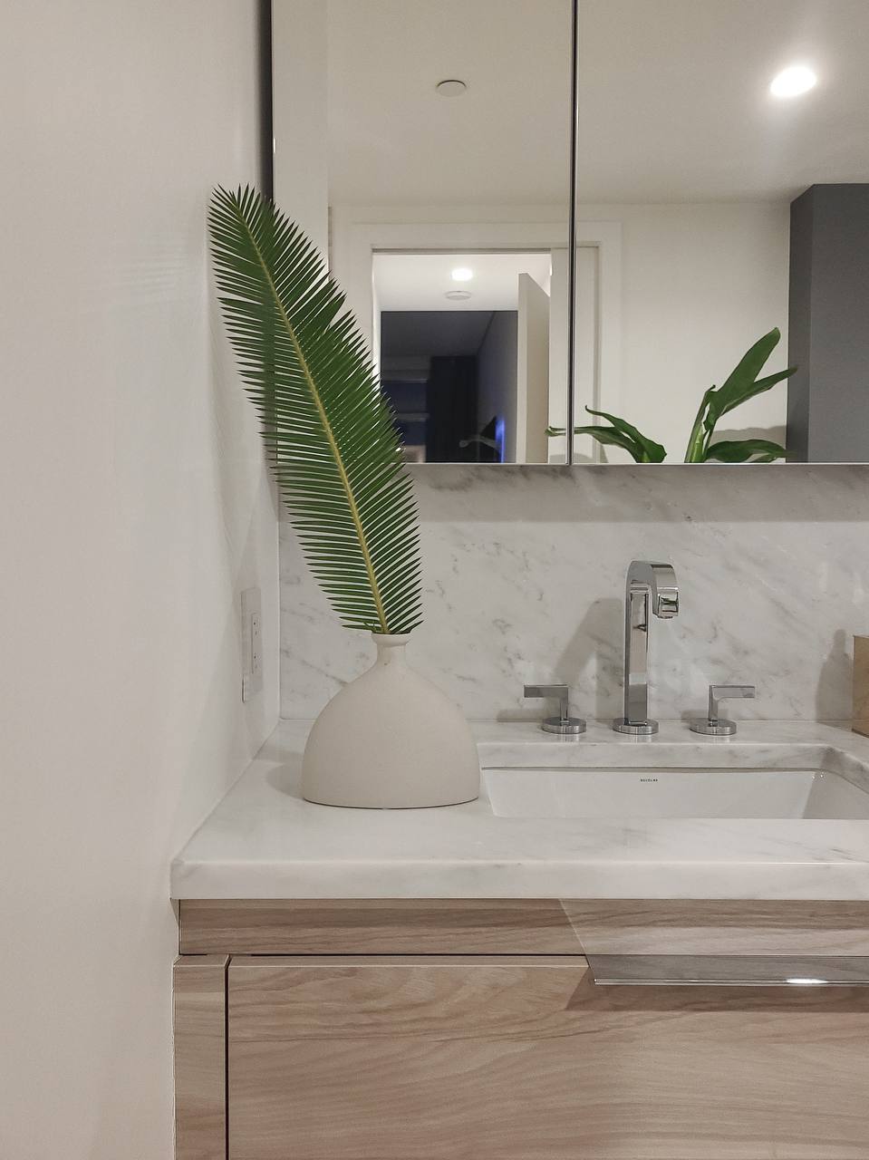 A single palm frond in a matte vase on a bathroom vanity