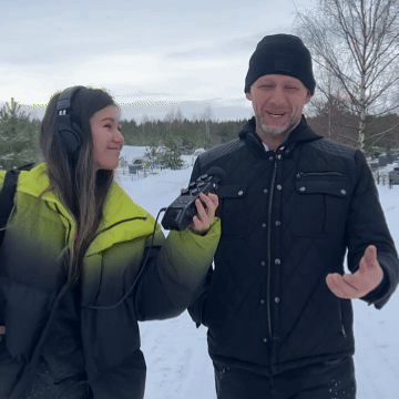 A journalist with headphones interviewing a man in a winter forest