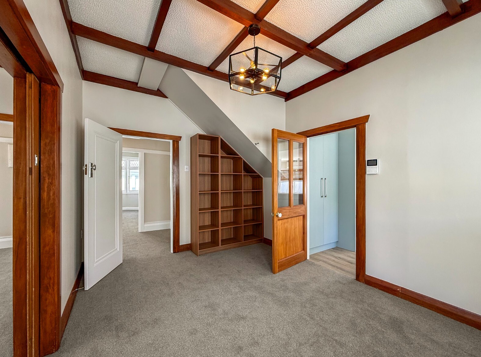 After renovation: refreshed room beneath the stairs with open shelving and grey carpet