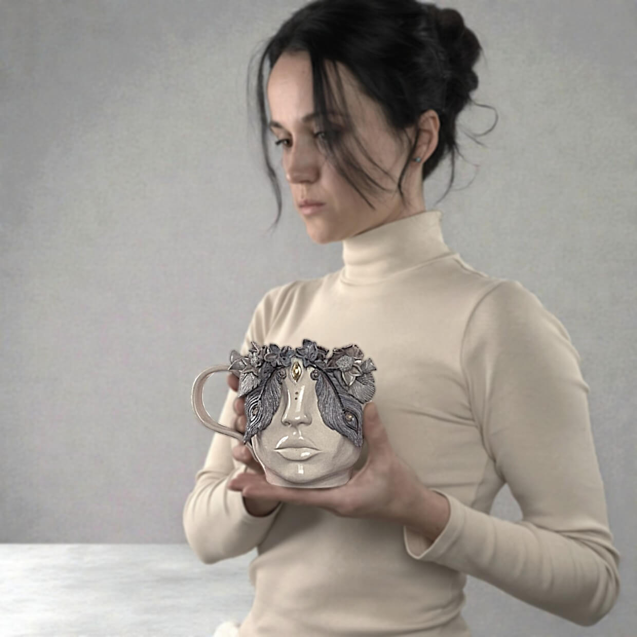 Unique handmade ceramic mug featuring a sculpted human face, textured floral crown, and detailed artistic relief elements