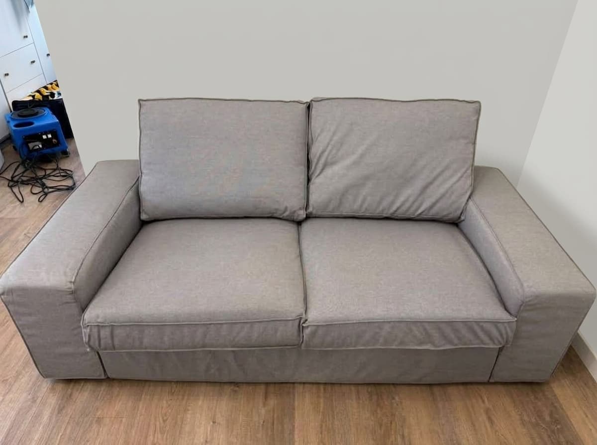 Dasselbe graue Mikrofaser-Sofa nach der Tiefenreinigung durch Shikardos Reinigung in Frankfurt &ndash; gleichm&auml;&szlig;ige Farbe ohne R&auml;nder, sichtbar gepflegter Stoff und frischer Geruch. Ein kleines Sofa mit zwei Sitzpl&auml;tzen wie dieses reinigen wir ab 130 Euro, Anfahrt inklusive.