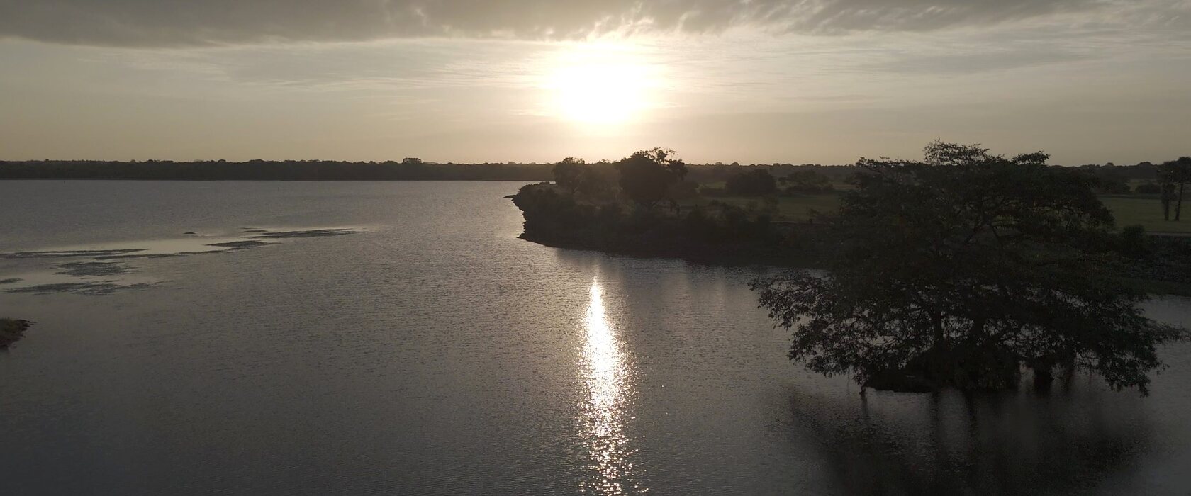 The tank at Punanai at low sun, trees standing in the shallows.