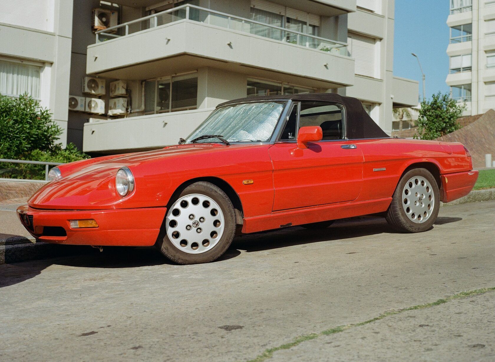 A classic red Alfa Romeo Spider on a winding road above Lake Como