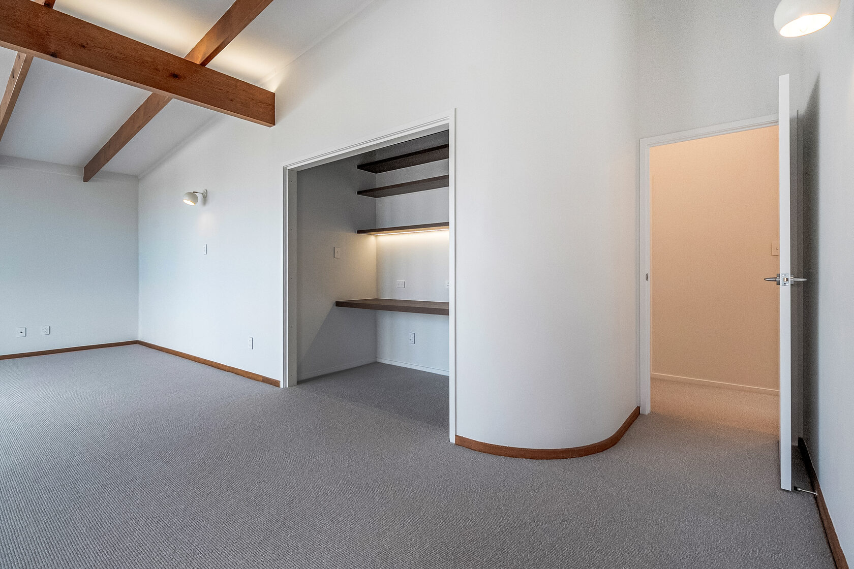 Modern living area with built-in desk nook, floating shelves with LED lighting, and exposed timber ceiling beams.