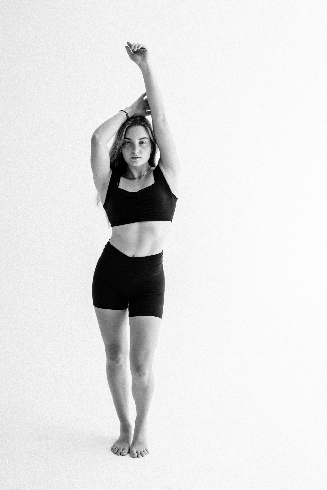 Barfüßiges Model in schwarzem Top und Shorts mit nach oben gestrecktem Arm