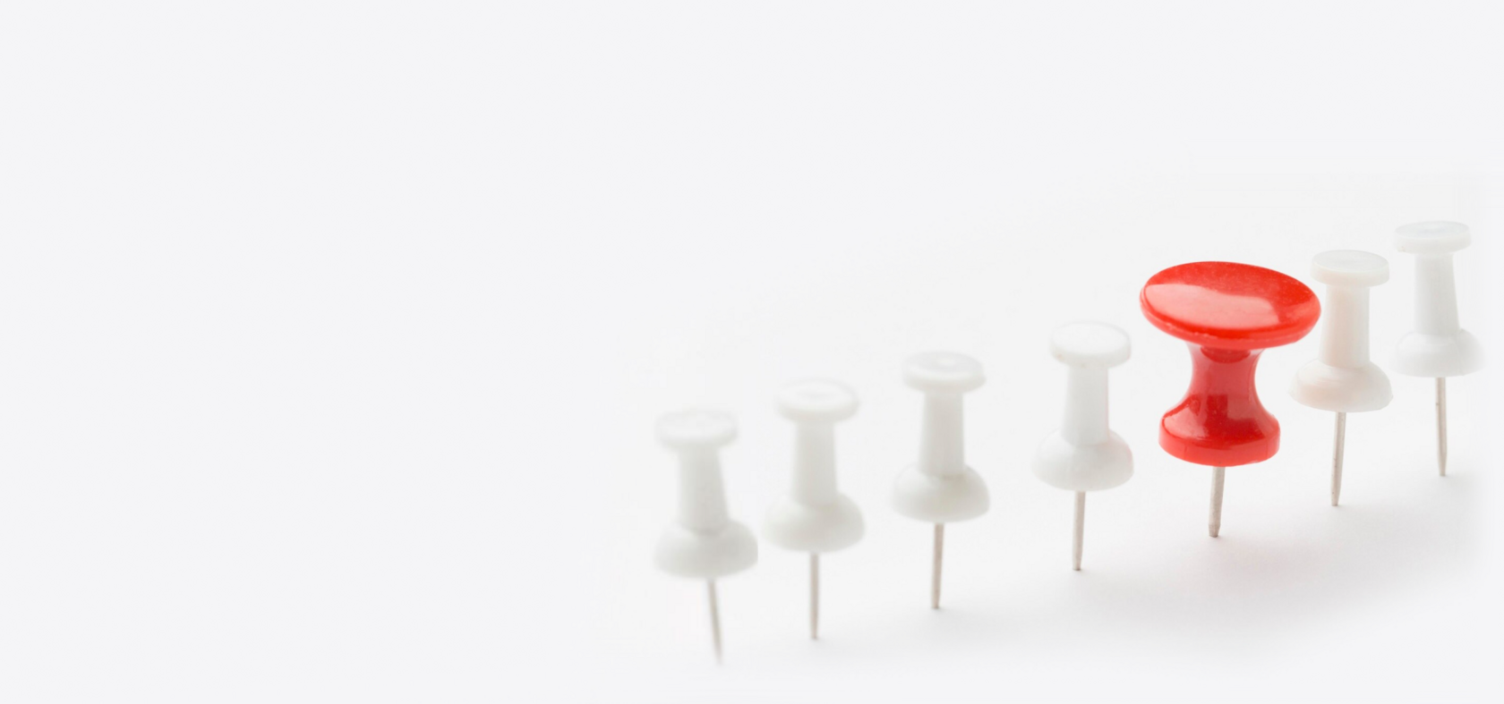 A row of seven push pins is displayed against a light background. Six are white, aligned in a diagonal line, while one near the center-right is red, standing out distinctly. Much like how you can easily hire Ruby developers to make your project shine.