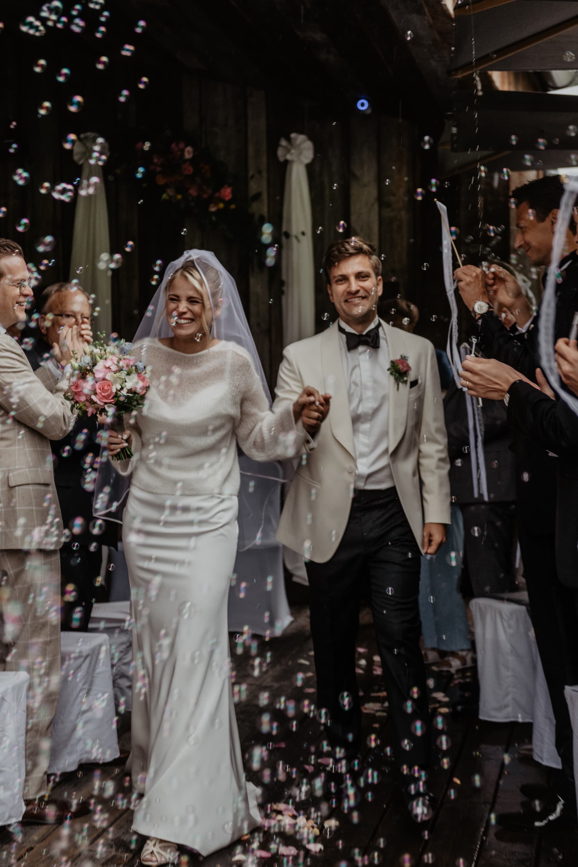 Newlyweds walking out of the ceremony through bubbles, guests cheering at a mountain wedding venue