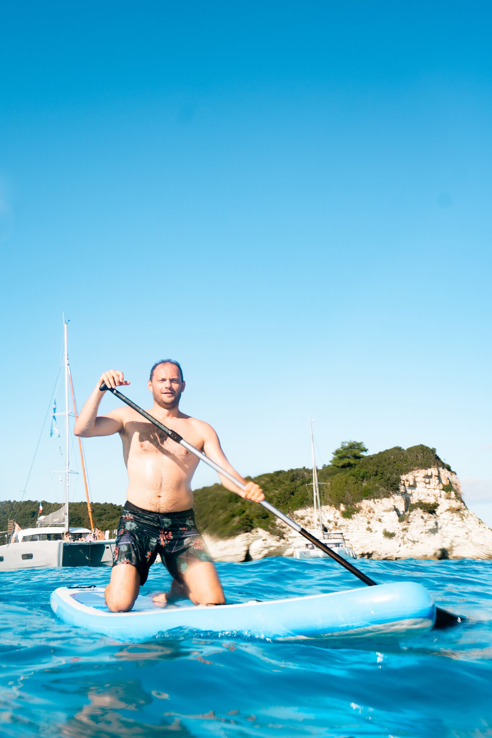Onur paddleboarding next to the anchored yachts
