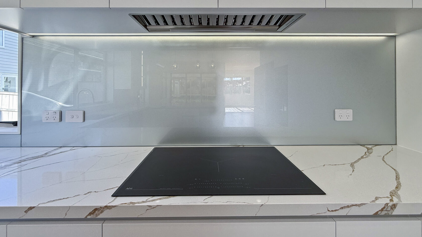 Induction cooktop, marble-look benchtop and glass splashback in the St Heliers kitchen.
