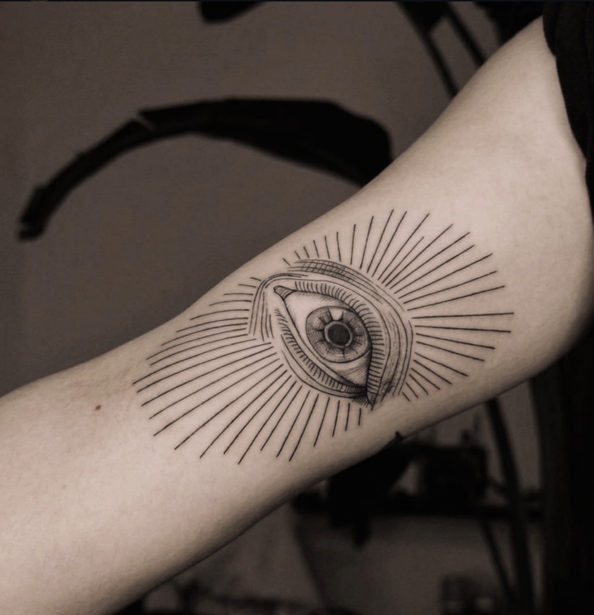 Inner-arm tattoo of an eye with lashes and a hatched iris, surrounded by straight radiating lines of varying lengths.