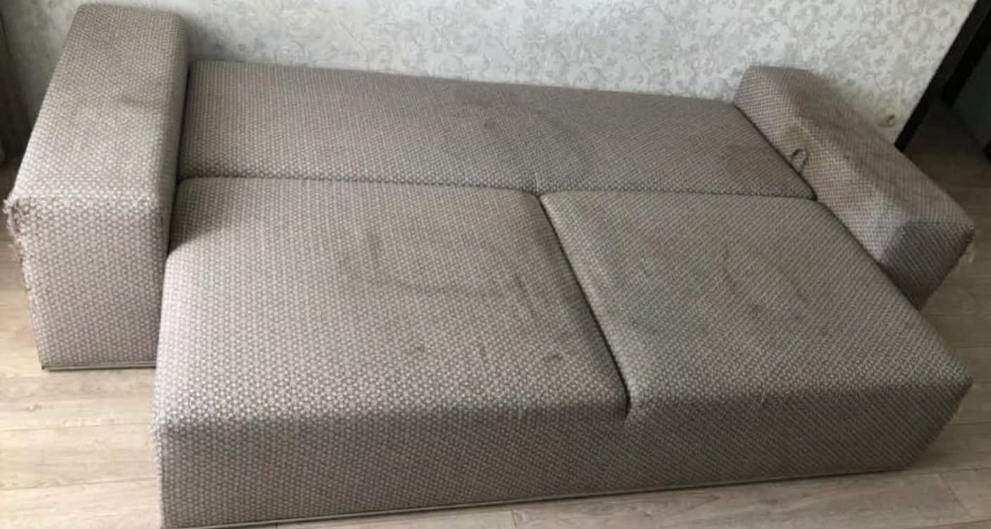Graues Stoffsofa vor der Reinigung, mit vielen Hundehaaren auf Sitzfl&auml;che und Kissen und einem unangenehmen Geruch im Polster. Die Kundin hat das Foto selbst aufgenommen und ihrer Google-Bewertung f&uuml;r Shikardos Reinigung in Frankfurt beigef&uuml;gt.